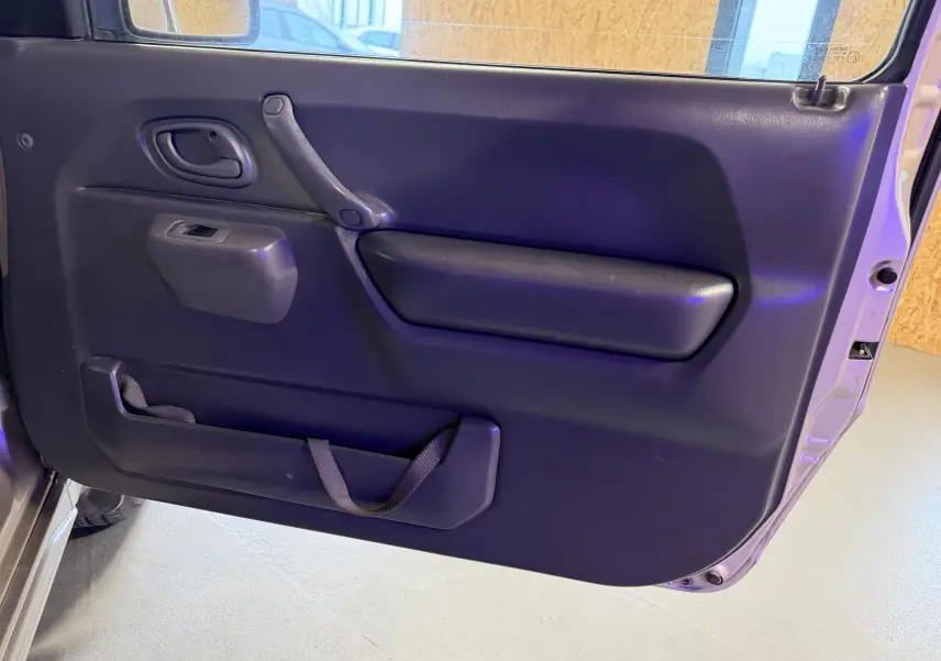 Vue intérieure de la porte côté gauche du Suzuki Jimny Cabriolet gris 2005, avec poignée et commande de vitre électrique.