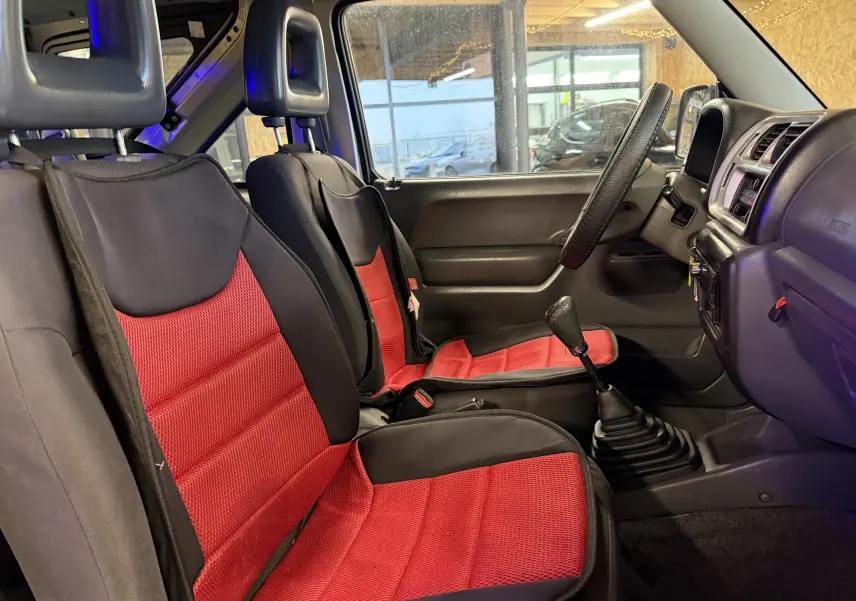 Intérieur du Suzuki Jimny Cabriolet 2005 vu côté conducteur, sièges rouges et noirs avec levier de vitesse manuel.