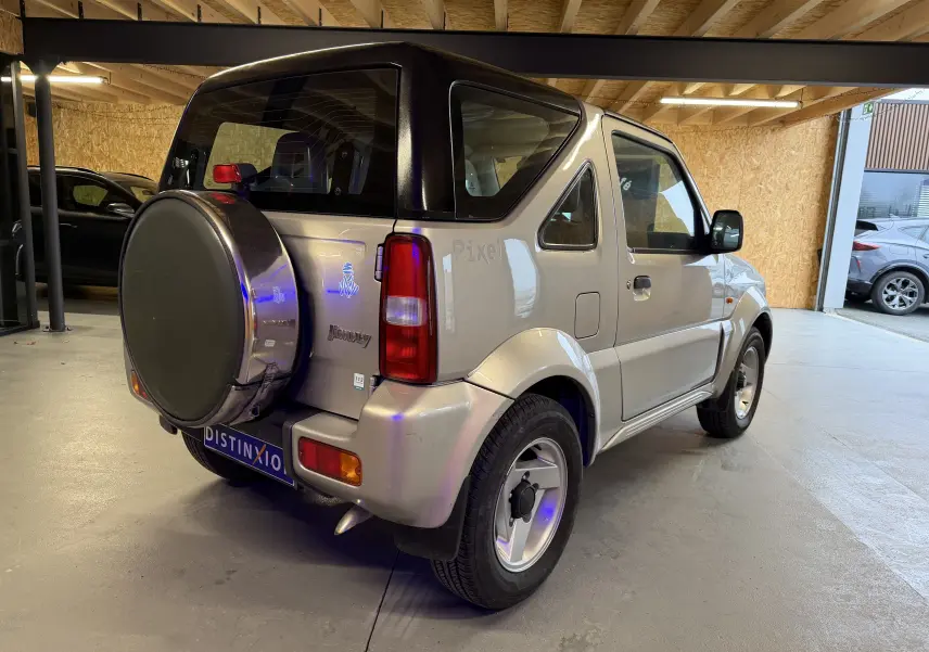 Vue 3/4 arrière droite d'un Suzuki Jimny Cabriolet gris 2005 avec roue de secours et jantes alu en intérieur.