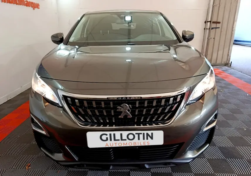 Peugeot 3008 gris foncé vue de face, mettant en valeur la calandre distinctive et les phares allumés.