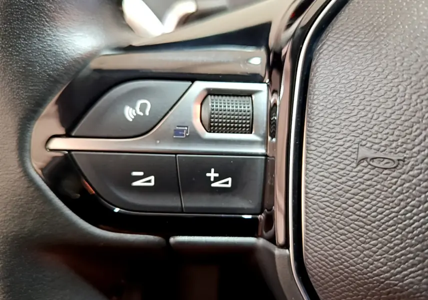 Gros plan sur les commandes gauche du volant cuir noir du Peugeot 3008 gris foncé, avec boutons de volume et téléphone.