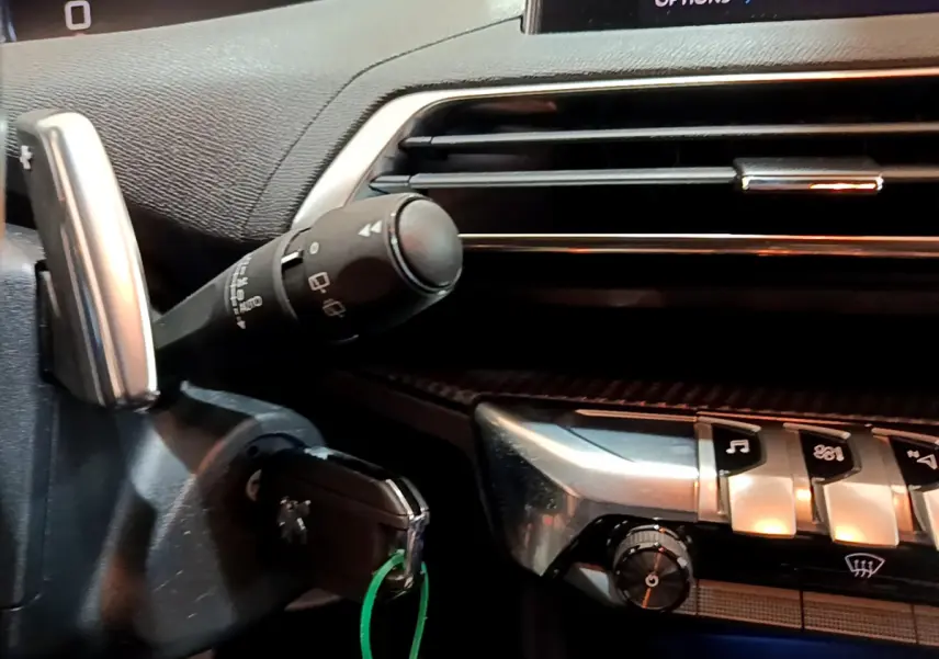 Détail du tableau de bord et commandes argentées du Peugeot 3008 gris foncé, avec clé insérée et touches fonctionnelles visibles.