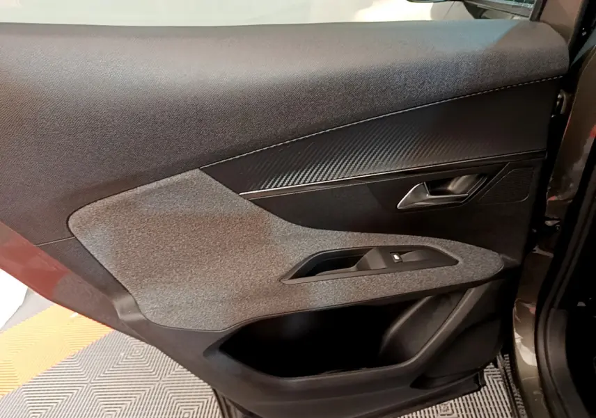 Gros plan sur la garniture intérieure de la porte avant droite du Peugeot 3008 gris foncé, avec insert effet carbone.