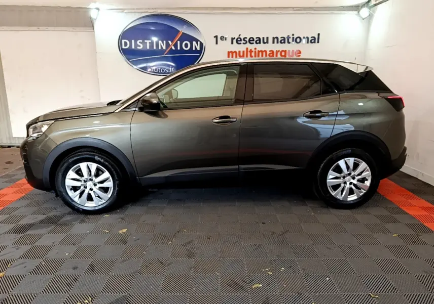 Profil côté gauche d'un Peugeot 3008 gris foncé 2020 dans un showroom avec sol en damier noir et rouge.