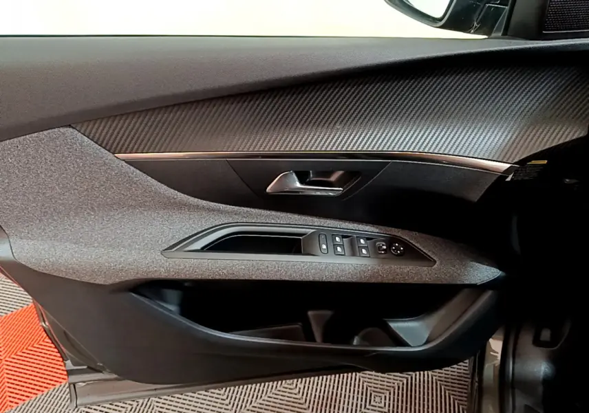Intérieur côté gauche de la porte d'une Peugeot 3008 gris foncé, avec commandes électriques et finition carbone.