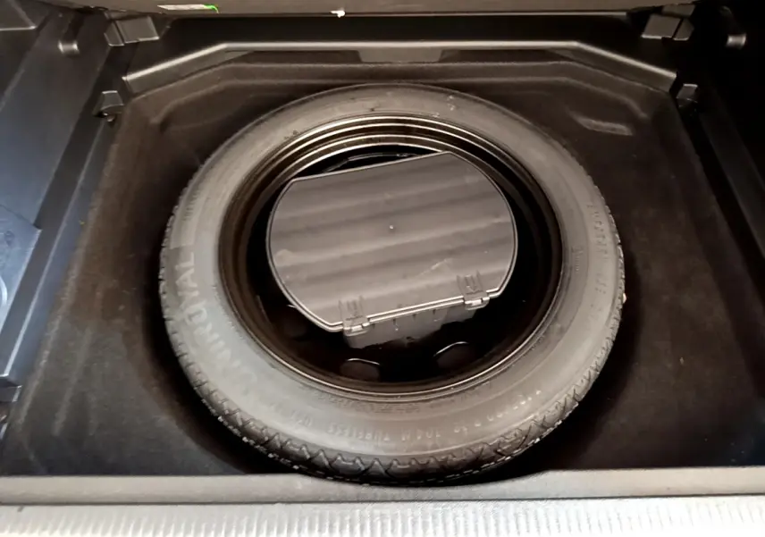 Roue de secours dans le coffre du Peugeot 3008 gris foncé, vue plongeante centrée sur le pneu de secours.
