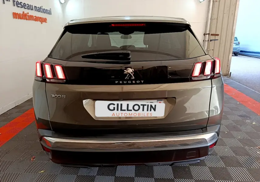 Vue arrière d'un Peugeot 3008 gris foncé avec feux arrière allumés et logo lion centré sur la malle.