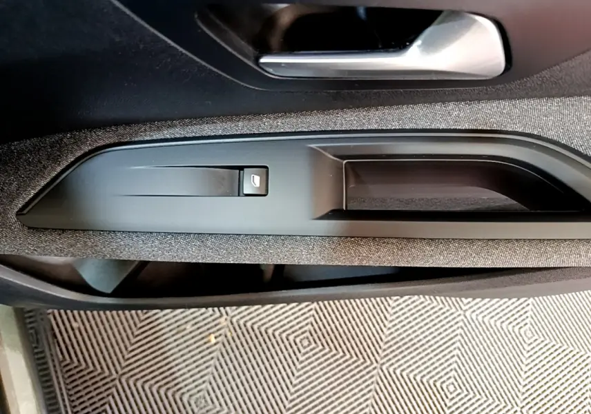 Poignée intérieure côté conducteur du Peugeot 3008 gris foncé, avec bouton de verrouillage des portes intégré.