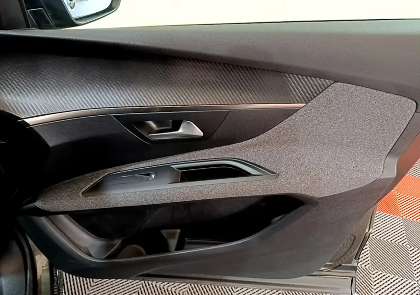 Gros plan sur la porte côté conducteur du Peugeot 3008 gris foncé, avec insert imitation carbone et commande de vitre.