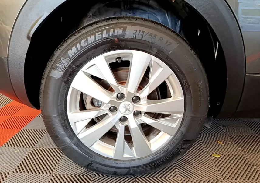 Gros plan sur la roue avant droite d’un Peugeot 3008 gris foncé, mettant en valeur la jante alliage et le pneu Michelin.