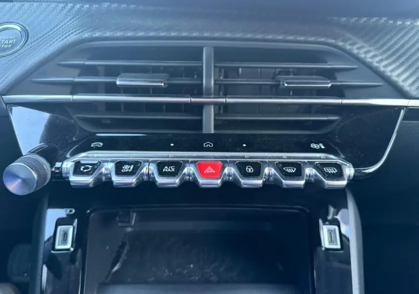 Gros plan sur la console centrale noire du Peugeot 208 Hybrid 110, montrant les boutons de commande et la grille d’aération.