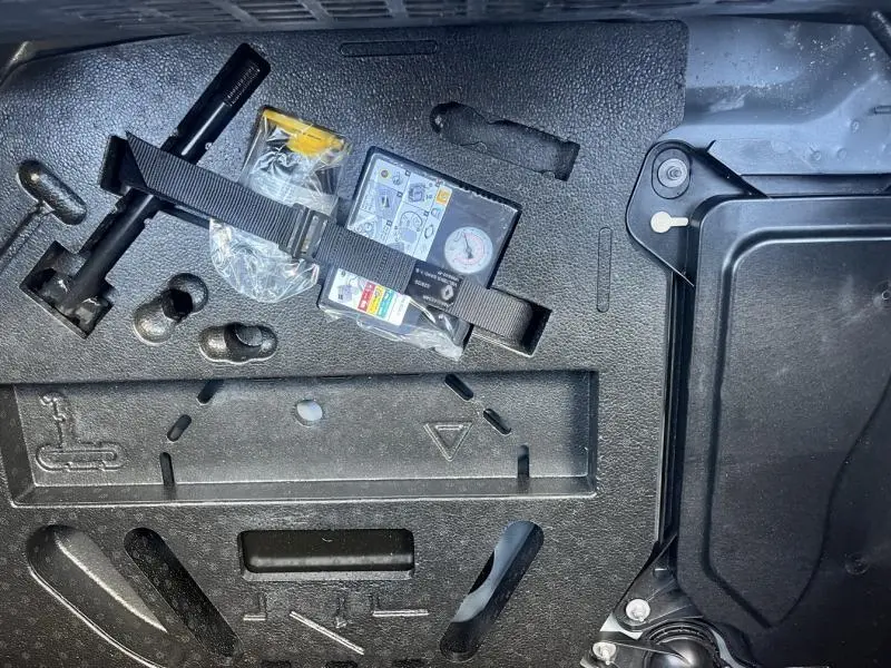 Gros plan sur le coffre de la Renault Clio 1.6 E-Tech 140ch Business gris Titanium, montrant le kit de réparation pneus et outils.