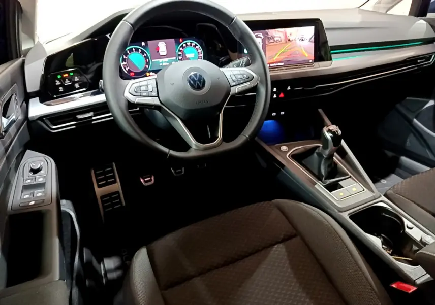 Intérieur avant d'une Volkswagen Golf 2022, vue du conducteur, volant cuir, écran tactile et levier de vitesse manuel visibles.