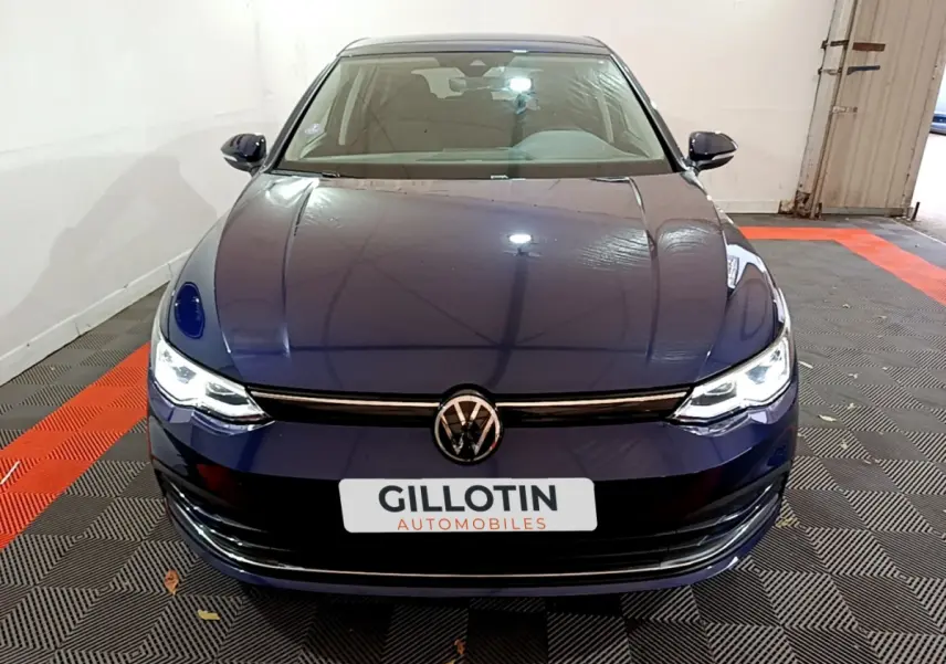 Vue frontale d'une Volkswagen Golf 1.0 TSI bleu foncé avec phares LED allumés dans un garage.