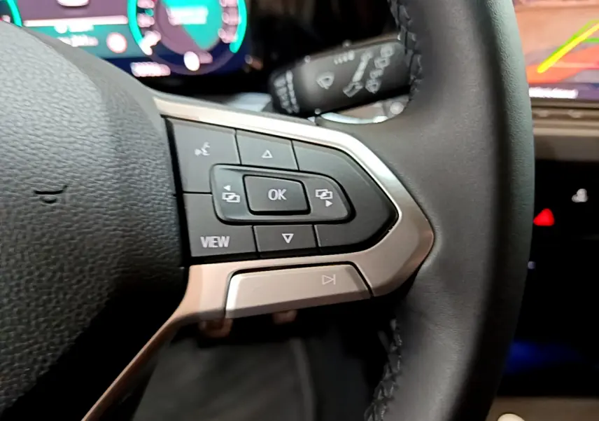 Gros plan sur les commandes gauche du volant cuir noir d'une Volkswagen Golf bleue, avec affichage numérique en arrière-plan.