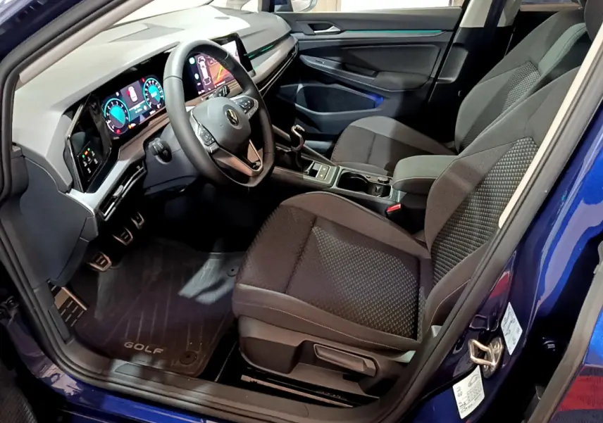 Vue intérieure côté conducteur d'une Volkswagen Golf bleu 2022 avec tableau de bord numérique et sièges noirs tissu.