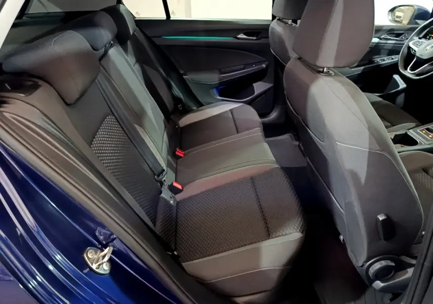 Vue intérieure côté gauche de la banquette arrière noire d'une Volkswagen Golf bleue 2022 avec éclairage d'ambiance bleu.