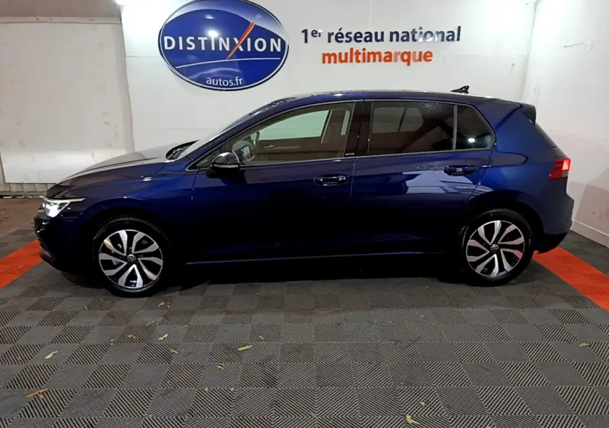 Profil côté gauche d'une Volkswagen Golf 1.0 TSI bleu foncé, avec jantes alliage et feux arrière allumés.