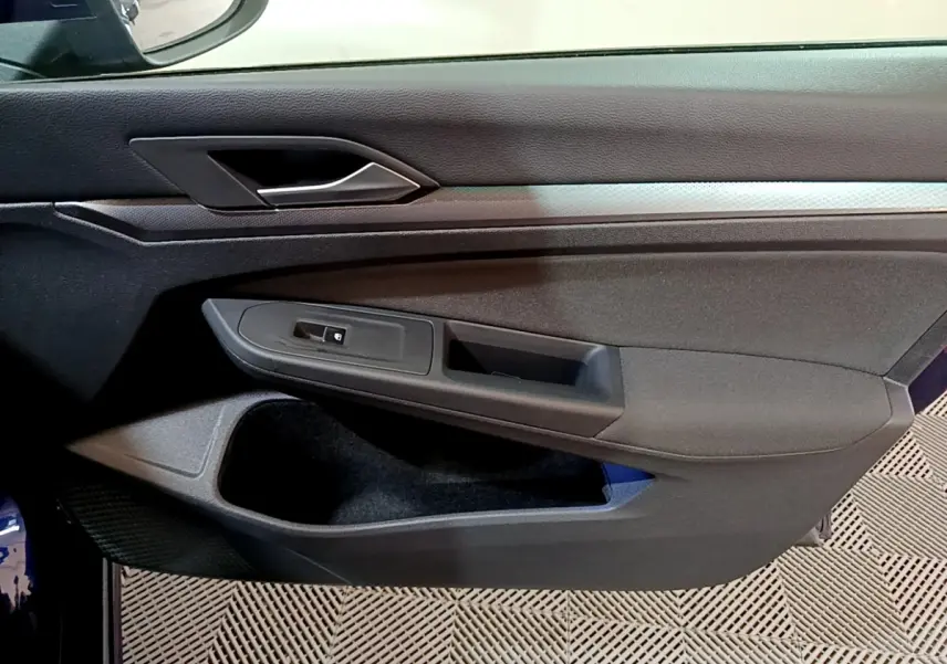 Vue rapprochée de la porte côté gauche d'une Volkswagen Golf bleu 2022, avec poignée et commande de vitre noire.