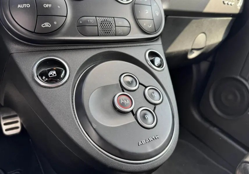 Gros plan sur la console centrale noire de l'Abarth 500 blanc, montrant les boutons de boîte auto avec logo Abarth.