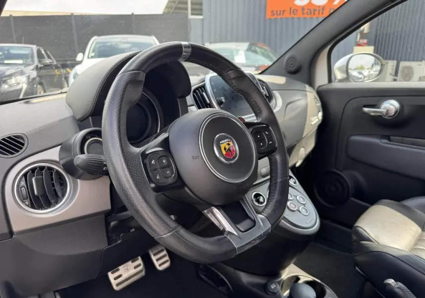 Intérieur de l'Abarth 500 blanc, vue côté conducteur sur le volant cuir avec logo Abarth et tableau de bord gris satiné.