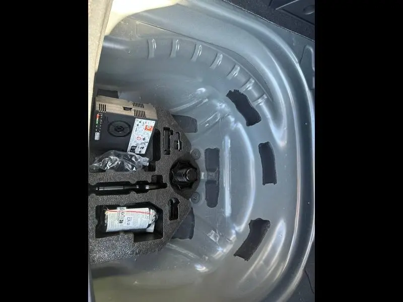 Coffre ouvert d’un SEAT LEON ST 2025 bleu saphir, vue plongeante sur le rangement sous plancher avec kit de réparation pneus.