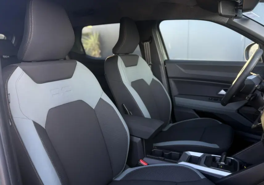 Vue intérieure côté conducteur du Dacia Duster 2026, sièges TEP MicroCloud gris clair et foncé avec accoudoir central.