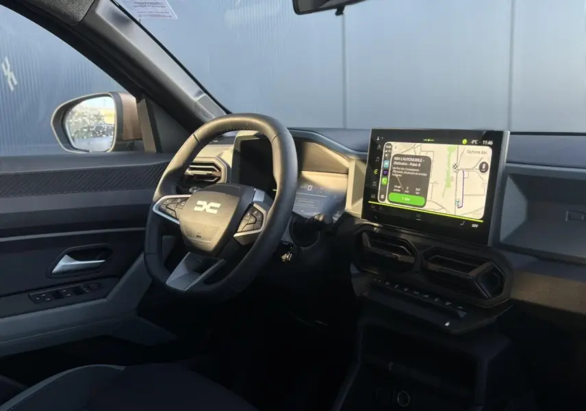 Vue intérieure côté conducteur du Dacia Duster 2026 gris, avec volant multifonction et écran tactile central affichant la navigation.