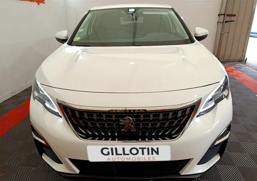 Vue frontale d'un Peugeot 3008 blanc avec calandre noire et phares LED allumés en intérieur showroom.