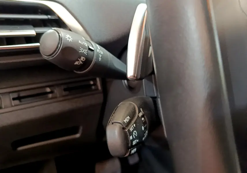 Gros plan sur les commandes au volant côté gauche d’un Peugeot 3008 blanc, montrant les réglages du régulateur de vitesse.