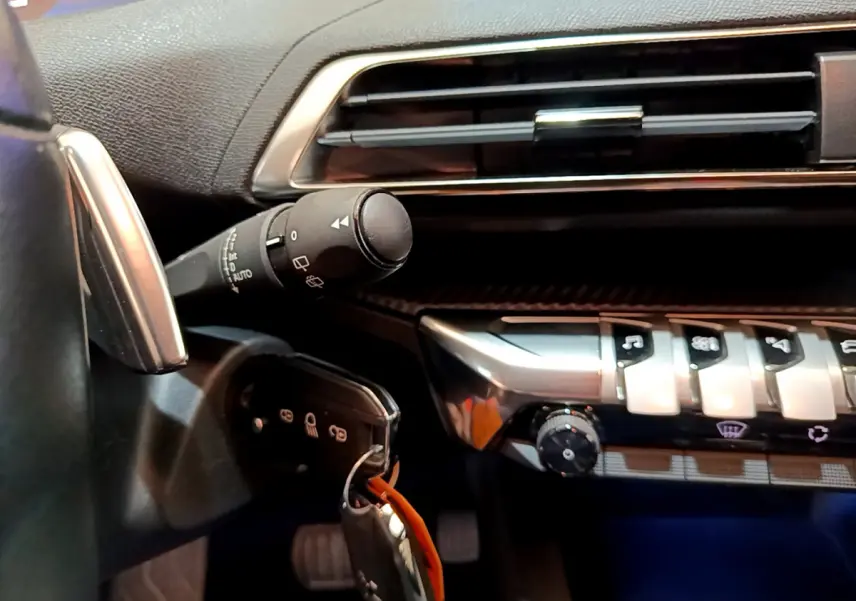 Gros plan sur la partie gauche du tableau de bord noir du Peugeot 3008 blanc, avec commandes et clé insérée.