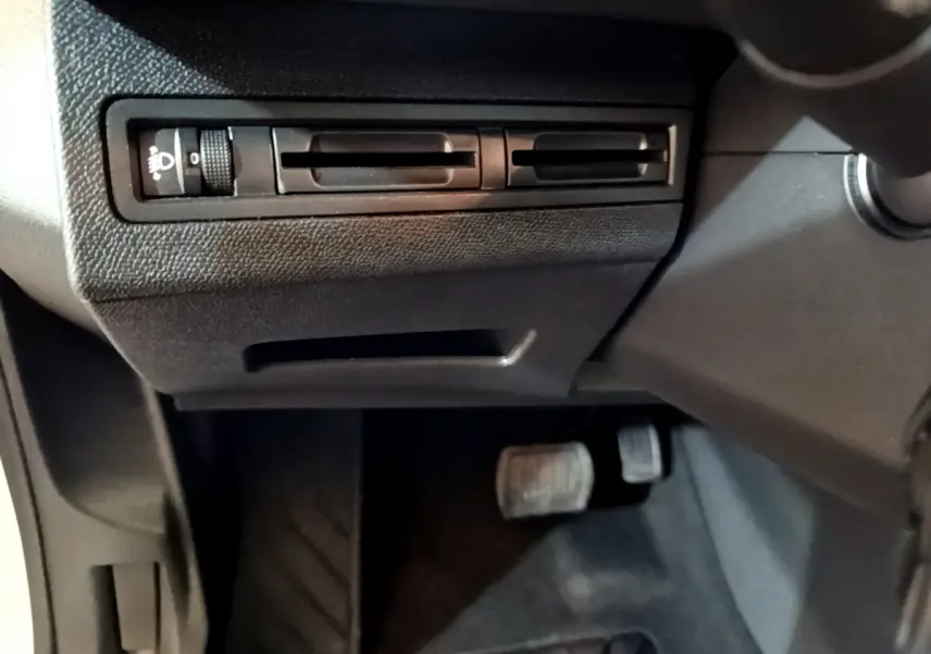 Vue rapprochée des commandes d'éclairage et des pédales côté conducteur dans l'habitacle noir du Peugeot 3008 blanc 2020.