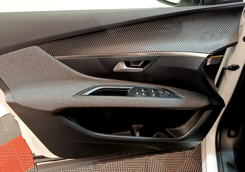 Vue intérieure côté gauche de la porte avant blanche du Peugeot 3008 avec commandes des vitres et insert effet carbone.