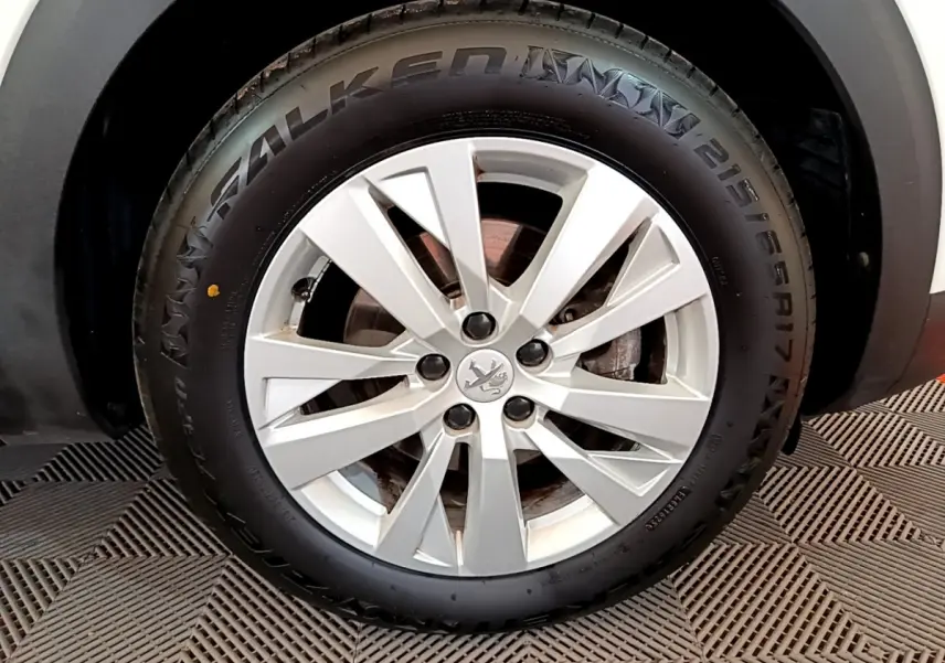Gros plan sur la roue avant droite d’un Peugeot 3008 blanc, mettant en valeur la jante alliage et le pneu Falken.