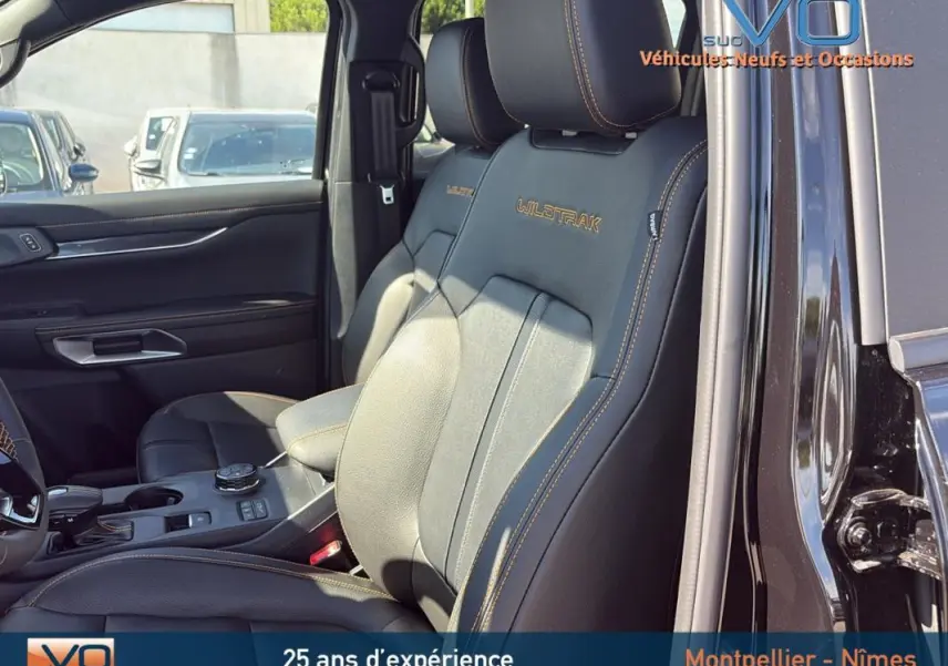Intérieur noir du Ford Ranger Wildtrak 2025 en vue latérale, sièges avant en cuir avec surpiqûres orange visibles.