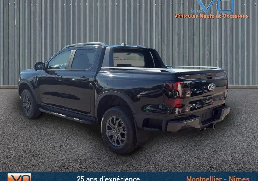 Ford Ranger Wildtrak noir vu en 3/4 arrière côté gauche, avec barres de toit et vitres surteintées.