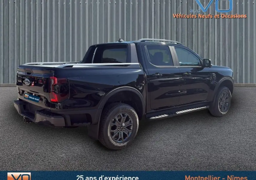 Ford Ranger Wildtrak noir en 3/4 arrière droit, avec barres de toit, marchepieds et jantes alliage 18 pouces.