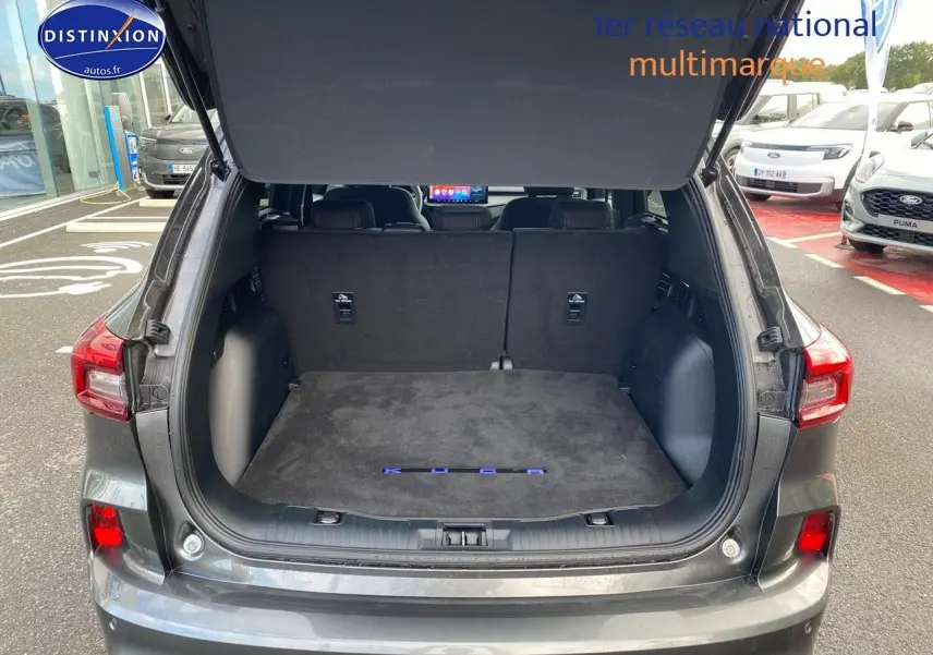 Vue arrière du Ford Kuga gris Magnetic avec coffre ouvert et tapis de coffre marqué KUGA visible.