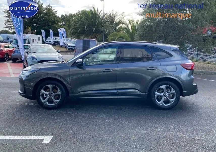 Vue de profil côté gauche d'un Ford Kuga 2025 gris métallisé garé en extérieur sur un parking.