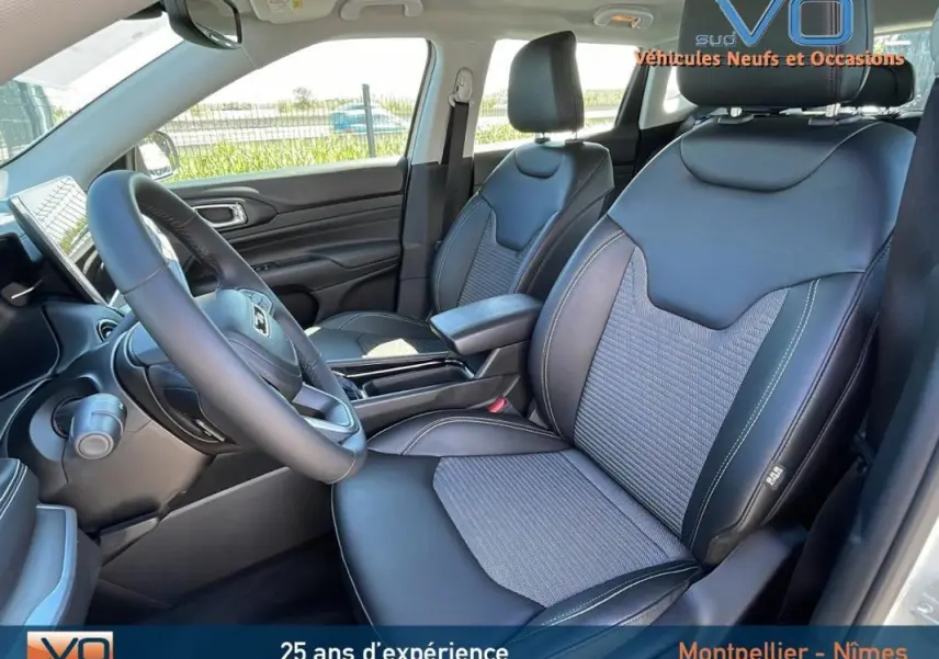 Vue intérieure côté conducteur du Jeep Compass blanc 2024, sièges en cuir noir avec accoudoir central et volant multifonction.