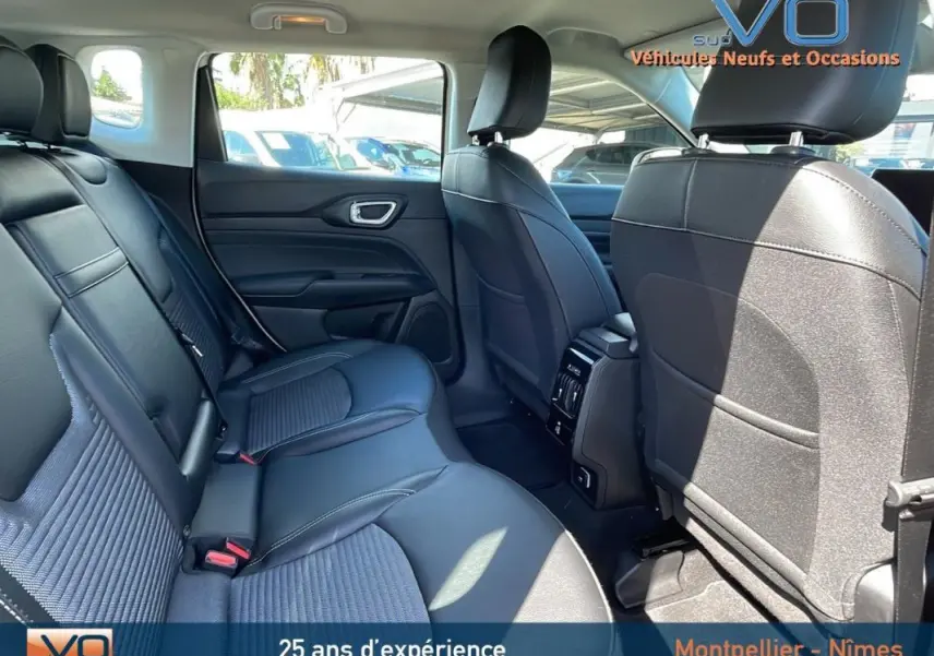 Vue intérieure arrière du Jeep Compass 2024 blanc, sièges noirs en cuir avec accoudoir central et prises USB visibles.