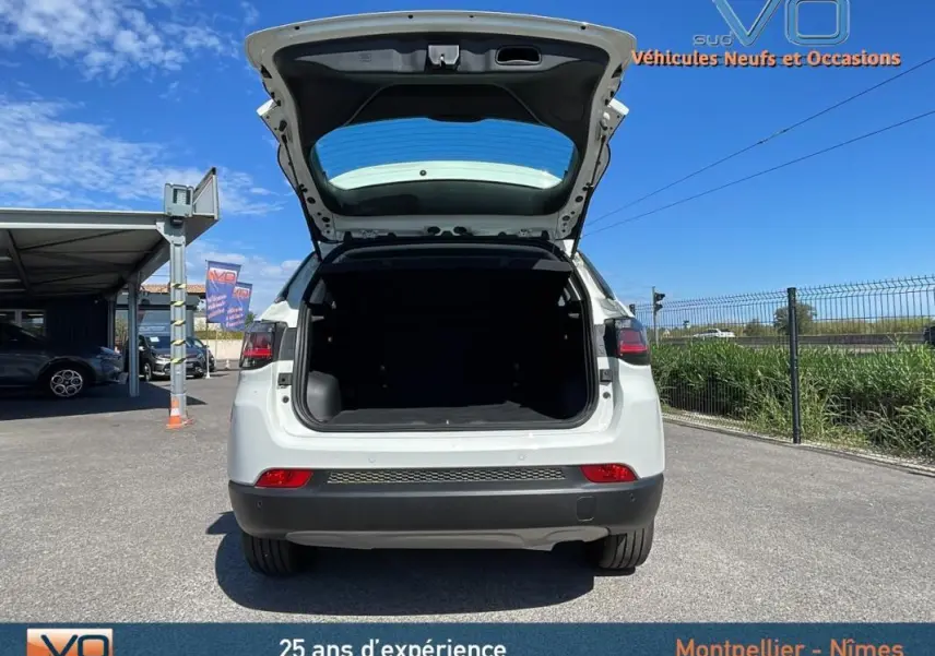 Vue arrière d'un Jeep Compass blanc 2024 avec coffre ouvert sur un parking ensoleillé