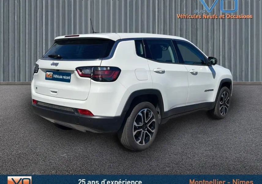 Jeep Compass blanc en 3/4 arrière droit, avec jantes alliage 18 pouces et vitres teintées sur fond urbain.