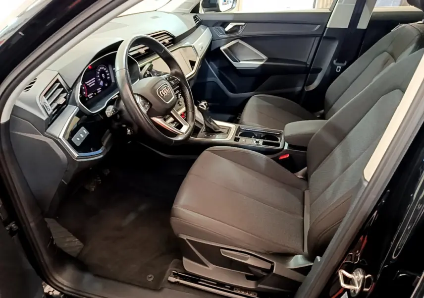 Intérieur côté conducteur d'Audi Q3 Sportback noir 2021, volant cuir, tableau de bord digital et sièges tissu gris.