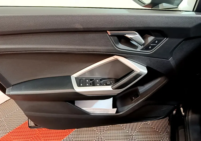 Vue intérieure côté gauche de la porte d'une Audi Q3 Sportback 2021 noire, avec commandes électriques et poignée argentée.