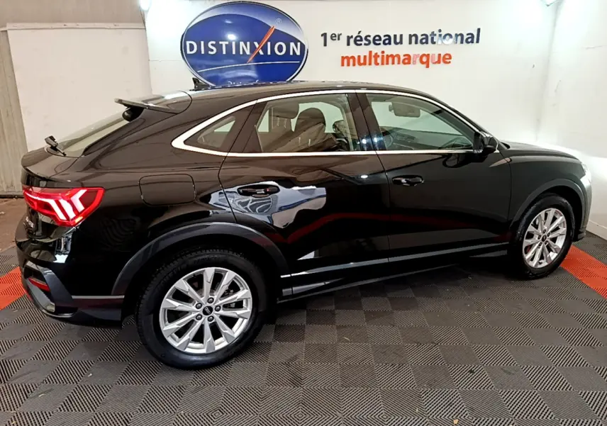 Audi Q3 Sportback noir vu de profil côté gauche, avec feux arrière LED allumés dans un showroom.