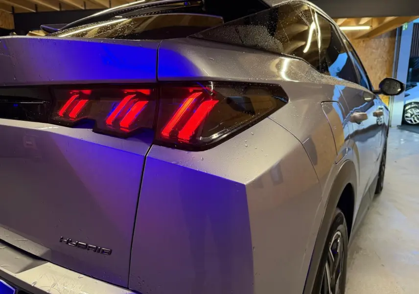 Vue 3/4 arrière droit du Peugeot 3008 gris 2025, mettant en valeur les feux arrière LED rouges et l'inscription Hybrid.