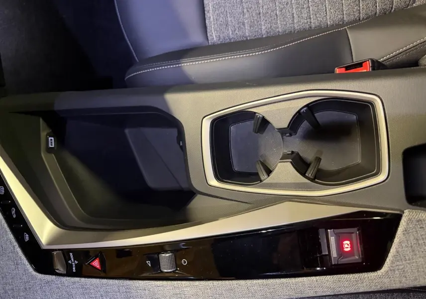 Gros plan sur la console centrale grise du Peugeot 3008 1.2 Hybrid 136 Allure avec porte-gobelets et bouton de frein à main électronique.