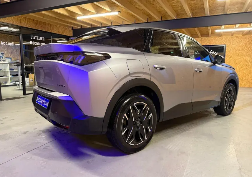 Vue 3/4 arrière droite du Peugeot 3008 gris hybride 2025, avec jantes noires et toit noir contrasté en intérieur d'atelier.