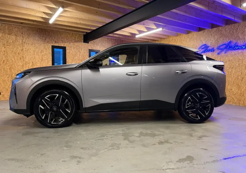 Vue de profil côté gauche du Peugeot 3008 gris 2025 avec jantes noires et toit noir dans un intérieur en bois.